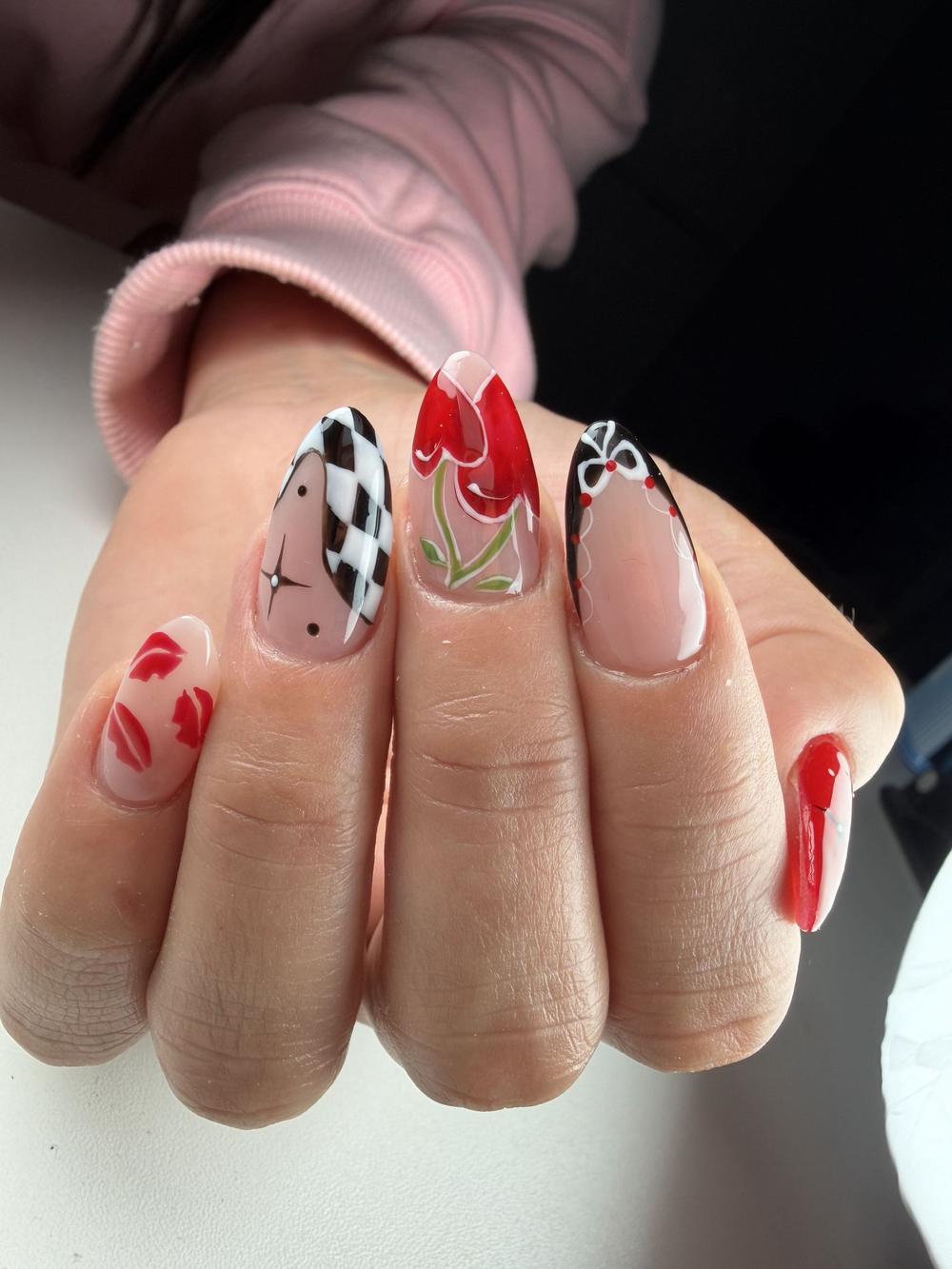 Close-up of almond-shaped nails with bold nail art: a black-and-white checkered pattern, a red floral design, and white bows with red dots — by Alice Garrido
